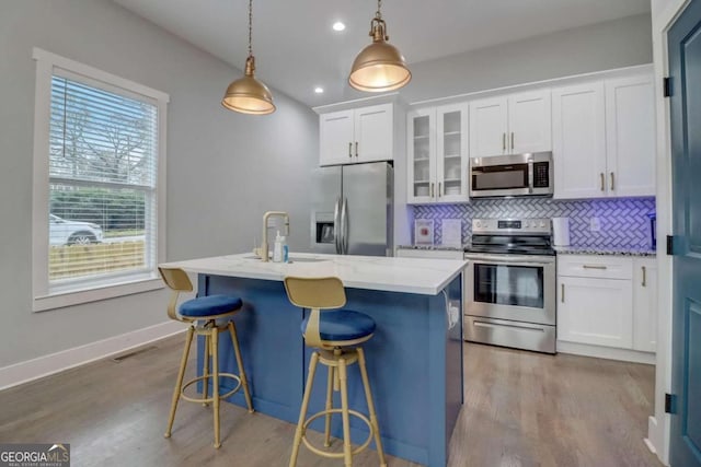 kitchen featuring pendant lighting, appliances with stainless steel finishes, a kitchen island with sink, hardwood / wood-style flooring, and white cabinetry