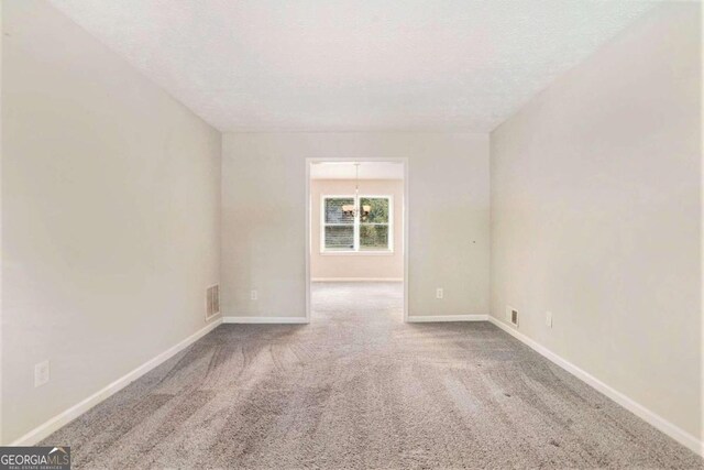 carpeted empty room with a chandelier and a textured ceiling