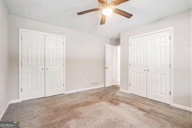 unfurnished bedroom featuring ceiling fan, carpet, a textured ceiling, and multiple closets