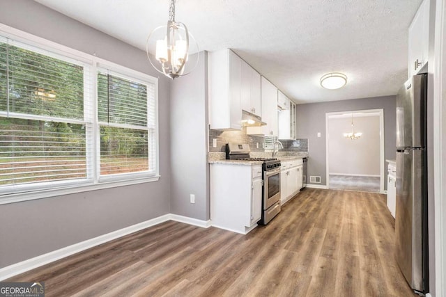 kitchen with backsplash, an inviting chandelier, stainless steel appliances, white cabinetry, and wood-type flooring