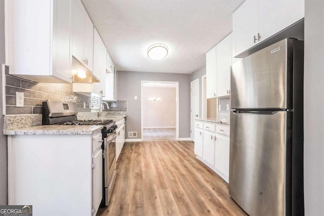 kitchen with backsplash, stainless steel appliances, white cabinetry, light stone counters, and light wood-type flooring