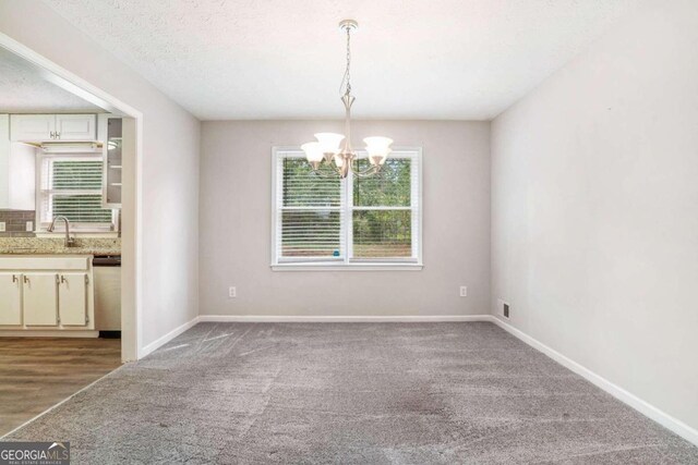 unfurnished dining area with an inviting chandelier, a healthy amount of sunlight, sink, and hardwood / wood-style flooring