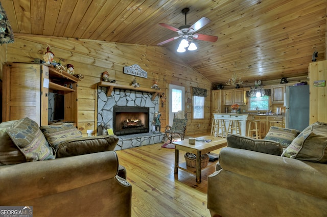 living room with vaulted ceiling, light hardwood / wood-style flooring, ceiling fan, and a stone fireplace