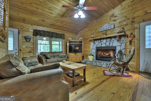 living room with wooden ceiling, wood-type flooring, a stone fireplace, wood walls, and ceiling fan