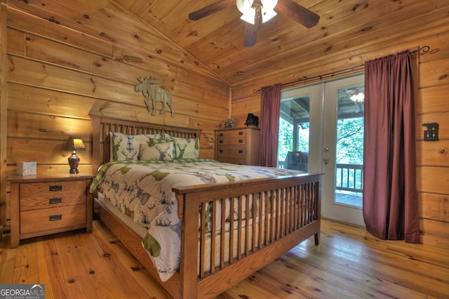 bedroom featuring wood walls, light hardwood / wood-style flooring, access to outside, lofted ceiling, and ceiling fan