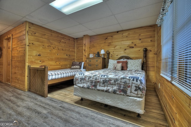 bedroom with a paneled ceiling, hardwood / wood-style flooring, and wooden walls