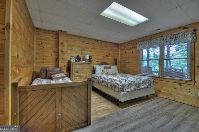 bedroom with hardwood / wood-style floors, a paneled ceiling, and wooden walls