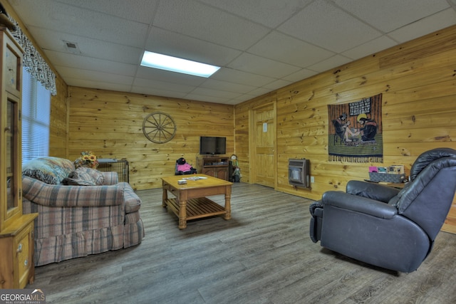 living room with wood walls, hardwood / wood-style flooring, heating unit, and a drop ceiling