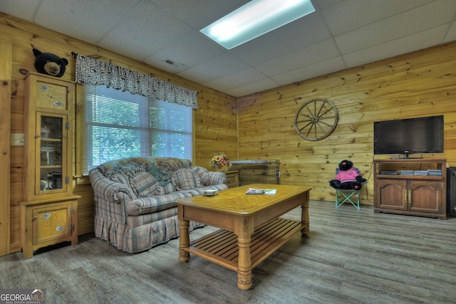 living room with wood-type flooring, wooden walls, and a drop ceiling