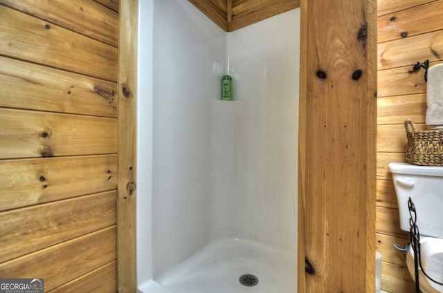 bathroom featuring walk in shower, toilet, and wooden walls