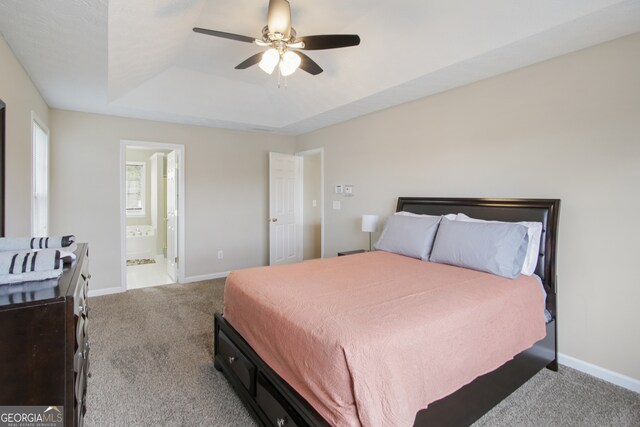 bedroom with a raised ceiling, ceiling fan, ensuite bath, and light carpet