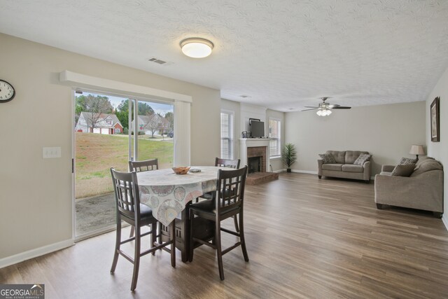 dining area featuring ceiling fan, hardwood / wood-style flooring, a textured ceiling, and a brick fireplace