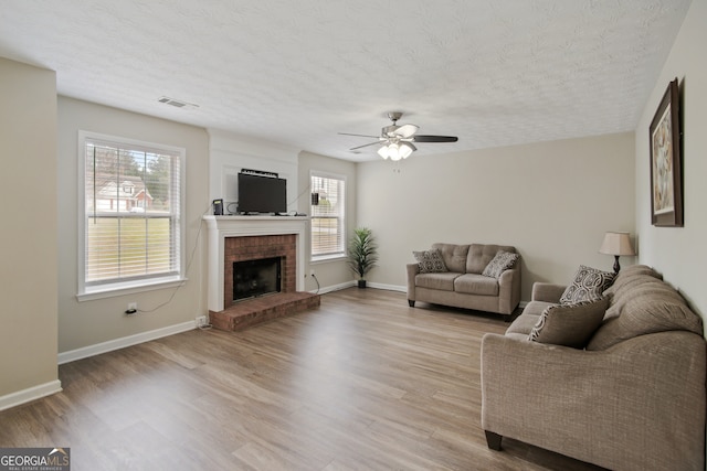 living room featuring plenty of natural light, ceiling fan, light wood-type flooring, and a brick fireplace