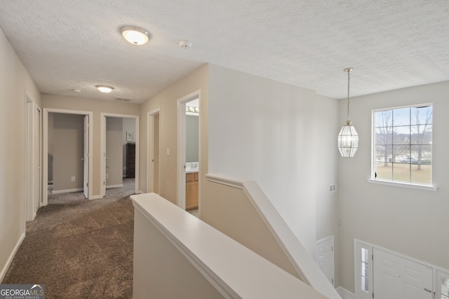 hallway featuring a textured ceiling and dark carpet