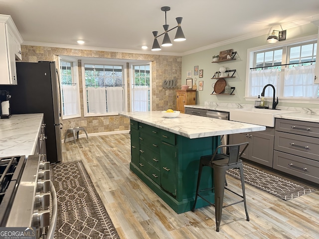 kitchen with ornamental molding, light hardwood / wood-style flooring, decorative light fixtures, sink, and white cabinets