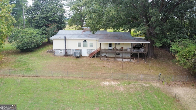 rear view of house with central AC, a wooden deck, and a lawn