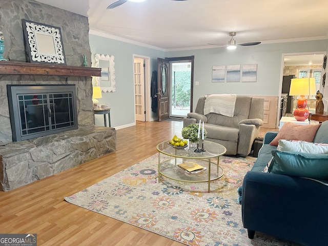 living room with light wood-type flooring, ceiling fan, a fireplace, and crown molding