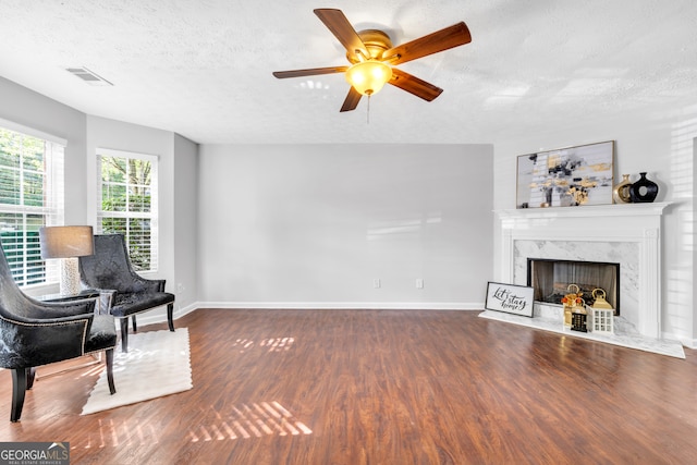 living area with a high end fireplace, wood-type flooring, a textured ceiling, and ceiling fan