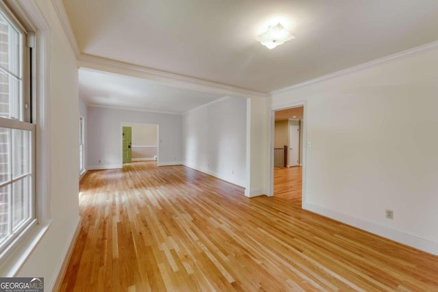 empty room with light wood-type flooring, baseboards, and ornamental molding