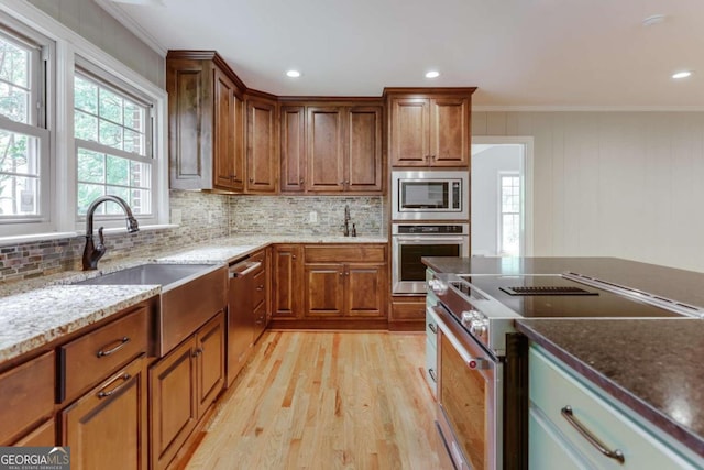 kitchen with stainless steel appliances, ornamental molding, light wood-type flooring, and dark stone counters