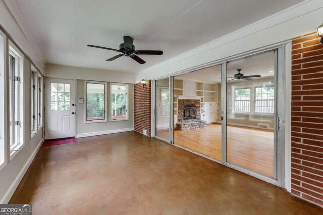 unfurnished sunroom featuring plenty of natural light, ceiling fan, and a brick fireplace