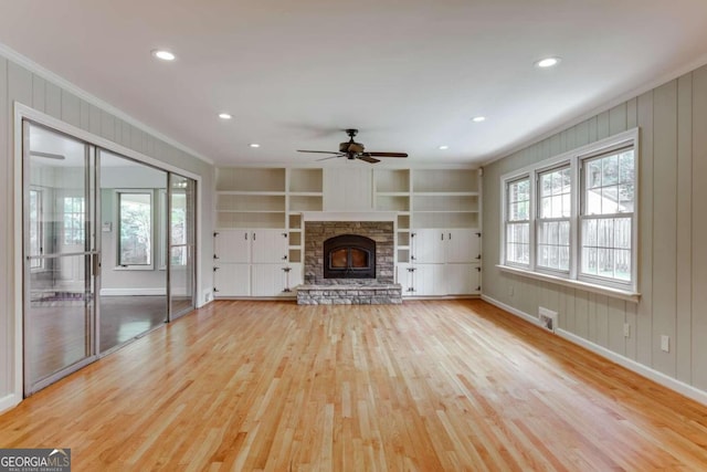 unfurnished living room featuring visible vents, built in features, a stone fireplace, light wood-style floors, and a ceiling fan