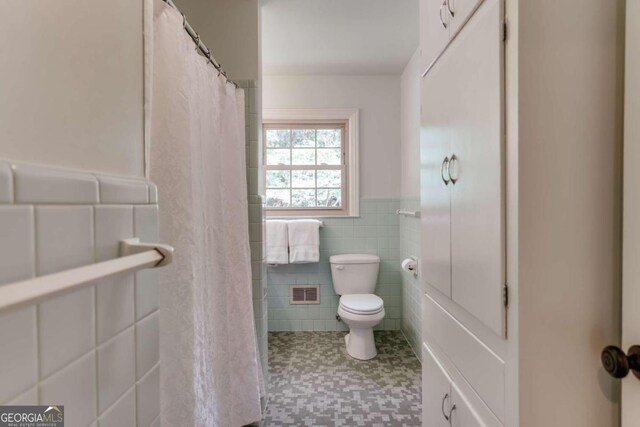 bathroom featuring curtained shower, tile walls, and toilet