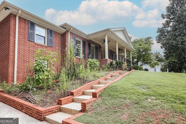 view of side of home featuring brick siding, stairway, a lawn, and a ceiling fan