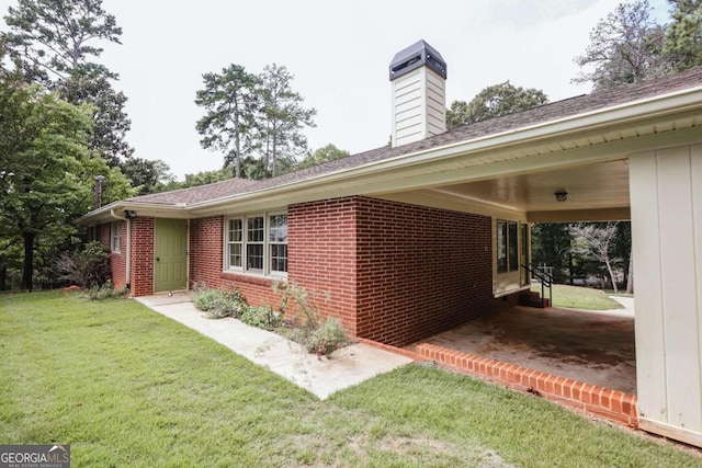 view of side of property featuring an attached carport, a lawn, brick siding, and a chimney