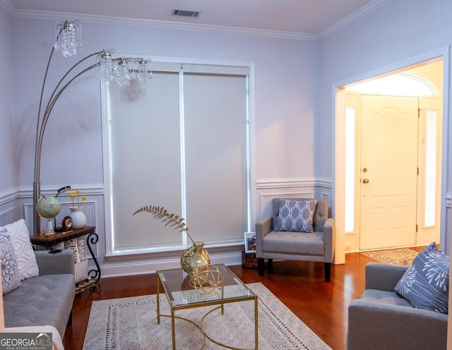 living room featuring a decorative wall, visible vents, crown molding, and wood finished floors