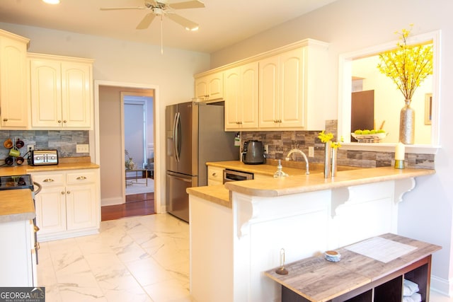 kitchen with a breakfast bar area, light countertops, a peninsula, stainless steel fridge, and marble finish floor