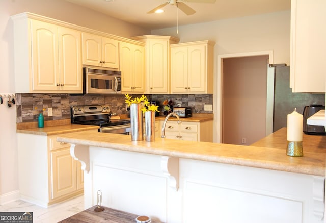 kitchen with a kitchen breakfast bar, backsplash, recessed lighting, appliances with stainless steel finishes, and light countertops