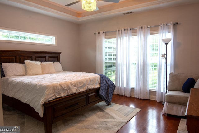 bedroom with visible vents, multiple windows, a tray ceiling, and wood finished floors