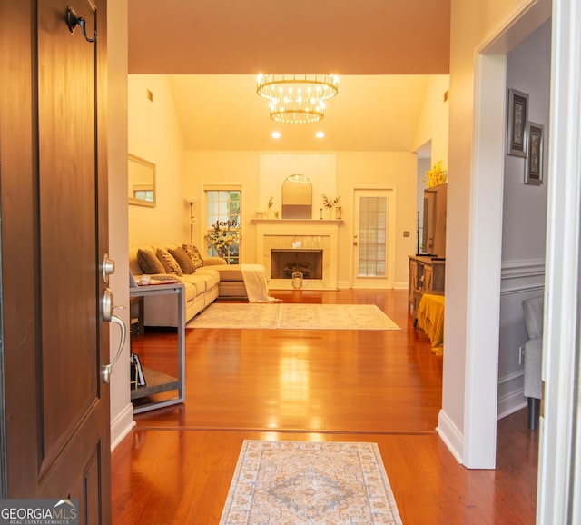 living area featuring lofted ceiling, wood finished floors, a high end fireplace, an inviting chandelier, and baseboards