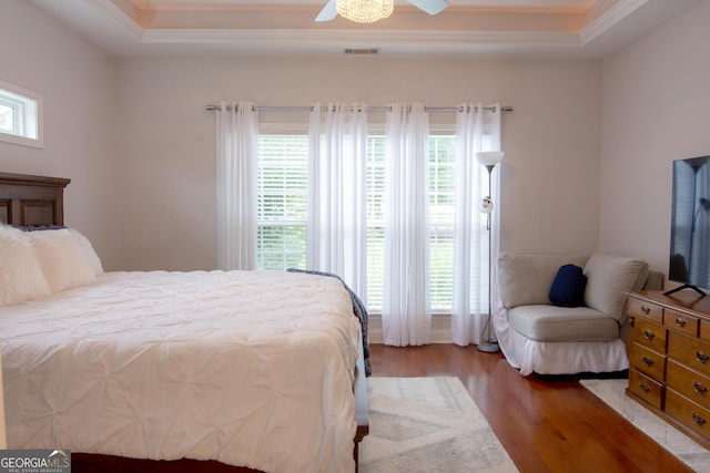 bedroom with visible vents, a raised ceiling, multiple windows, and wood finished floors