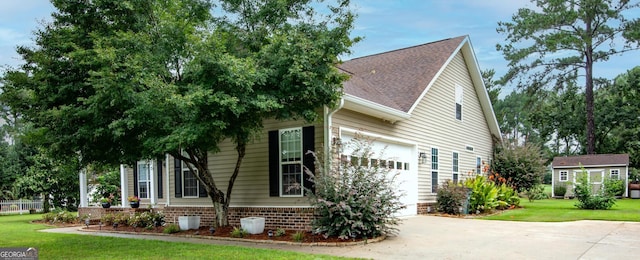 view of side of home with concrete driveway, roof with shingles, a lawn, a garage, and an outbuilding