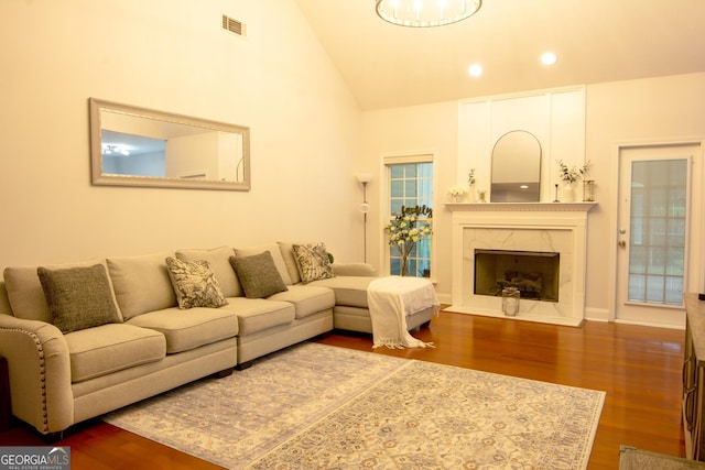 living area featuring a high end fireplace, visible vents, recessed lighting, wood finished floors, and high vaulted ceiling