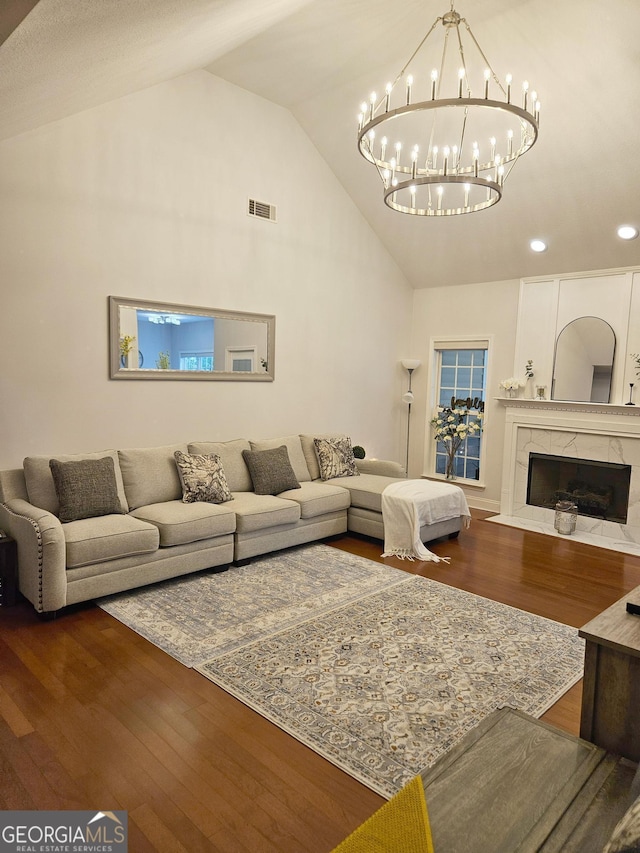 living area with visible vents, a premium fireplace, an inviting chandelier, wood finished floors, and high vaulted ceiling