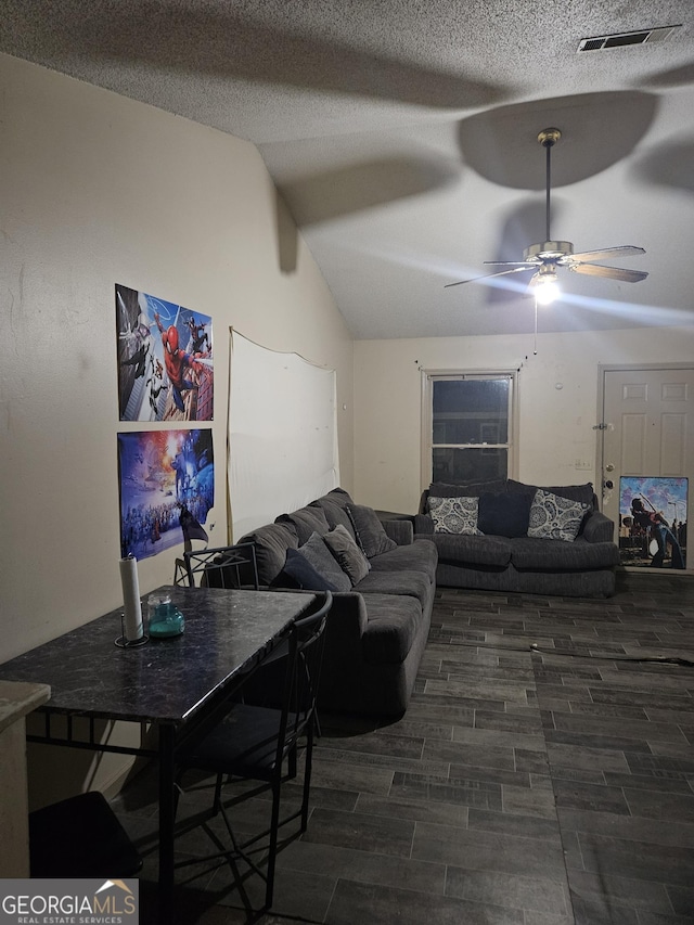 living room featuring ceiling fan, vaulted ceiling, dark wood-type flooring, and a textured ceiling