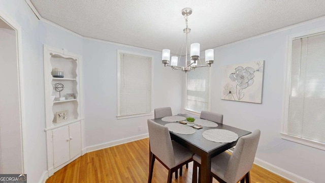 dining area with a textured ceiling, ornamental molding, an inviting chandelier, and light hardwood / wood-style floors