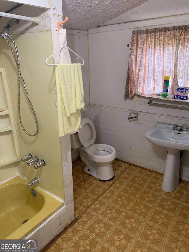 bathroom featuring a textured ceiling, toilet, and wooden walls