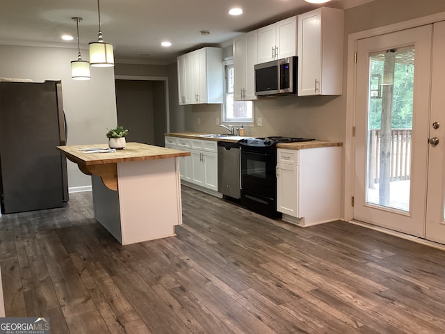 kitchen featuring appliances with stainless steel finishes, butcher block countertops, a center island, decorative light fixtures, and white cabinets