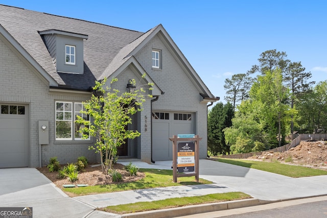 view of front of property featuring a garage, driveway, brick siding, and roof with shingles