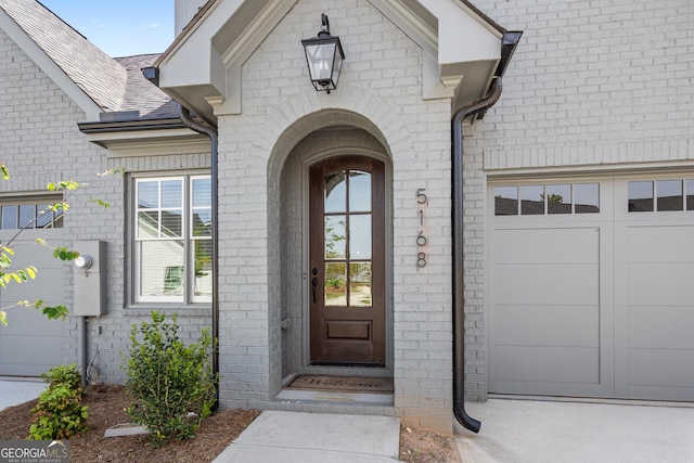 property entrance featuring an attached garage, a shingled roof, and brick siding