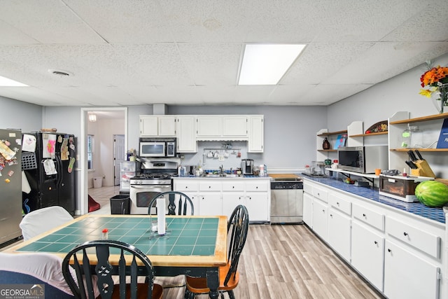 kitchen with white cabinets, appliances with stainless steel finishes, light wood-type flooring, tile counters, and sink