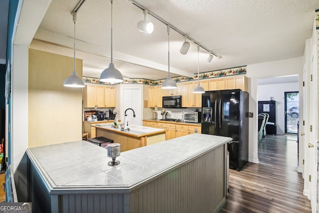 kitchen with black appliances, an island with sink, pendant lighting, light brown cabinets, and dark hardwood / wood-style floors