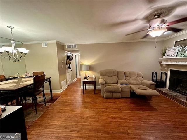 living room with ornamental molding, dark hardwood / wood-style floors, ceiling fan with notable chandelier, and a fireplace