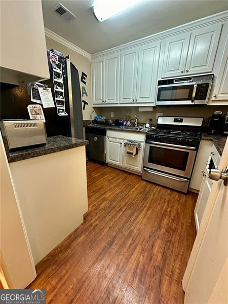 kitchen featuring stainless steel appliances, dark hardwood / wood-style flooring, and crown molding