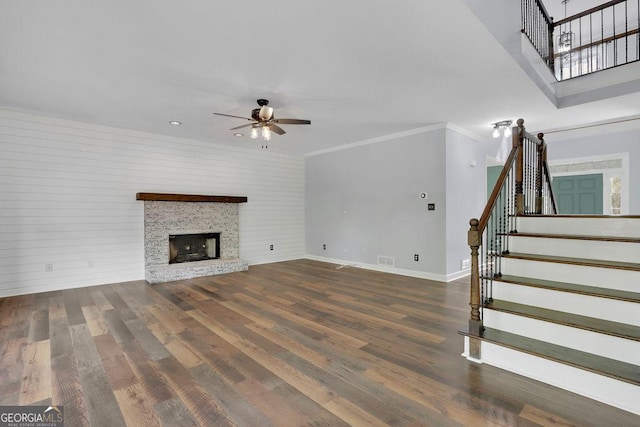 unfurnished living room with ceiling fan, dark hardwood / wood-style flooring, a stone fireplace, and crown molding