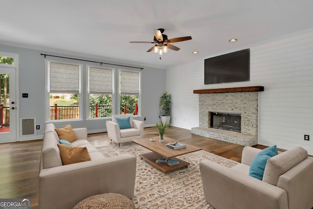 living room featuring wood walls, ceiling fan, ornamental molding, a fireplace, and light hardwood / wood-style floors